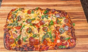 Pizza in teglia con cornicione alto, lievitata perfettamente, pronta da servire su un tavolo.