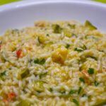 Risotto alla milanese cremoso, con una spolverata di parmigiano e zafferano, servito in un piatto bianco.
