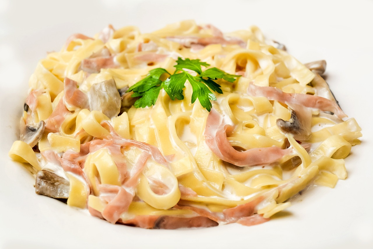 Pasta con panna e prosciutto in un piatto, guarnita con prezzemolo fresco.
