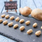 Gnocchi di patate freschi su un piano di lavoro con ingredienti e attrezzi per la preparazione.