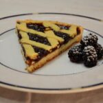 Crostata alla marmellata appena sfornata su un tavolo di legno, decorata con strisce di pasta frolla.