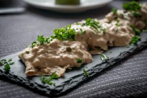 Piatto di vitello tonnato con salsa di tonno, decorato con capperi e fette di carne.
