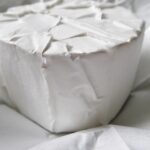 Formaggio avvolto in carta forno, posizionato su un ripiano di un frigorifero.