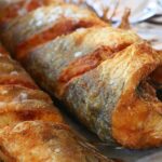 Frittura di pesce dorato e croccante su un piatto, con limone e prezzemolo decorativi.