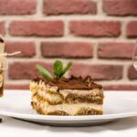 Fetta di tiramisù originale con crema e cacao, su piatto bianco decorato.