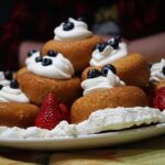 Babà al rum su un piatto, soffice e dorato, decorato con crema e frutta, simbolo della tradizione napoletana.