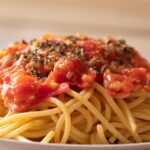 Pasta al pomodoro servita con basilico fresco e parmigiano grattugiato su un piatto bianco.