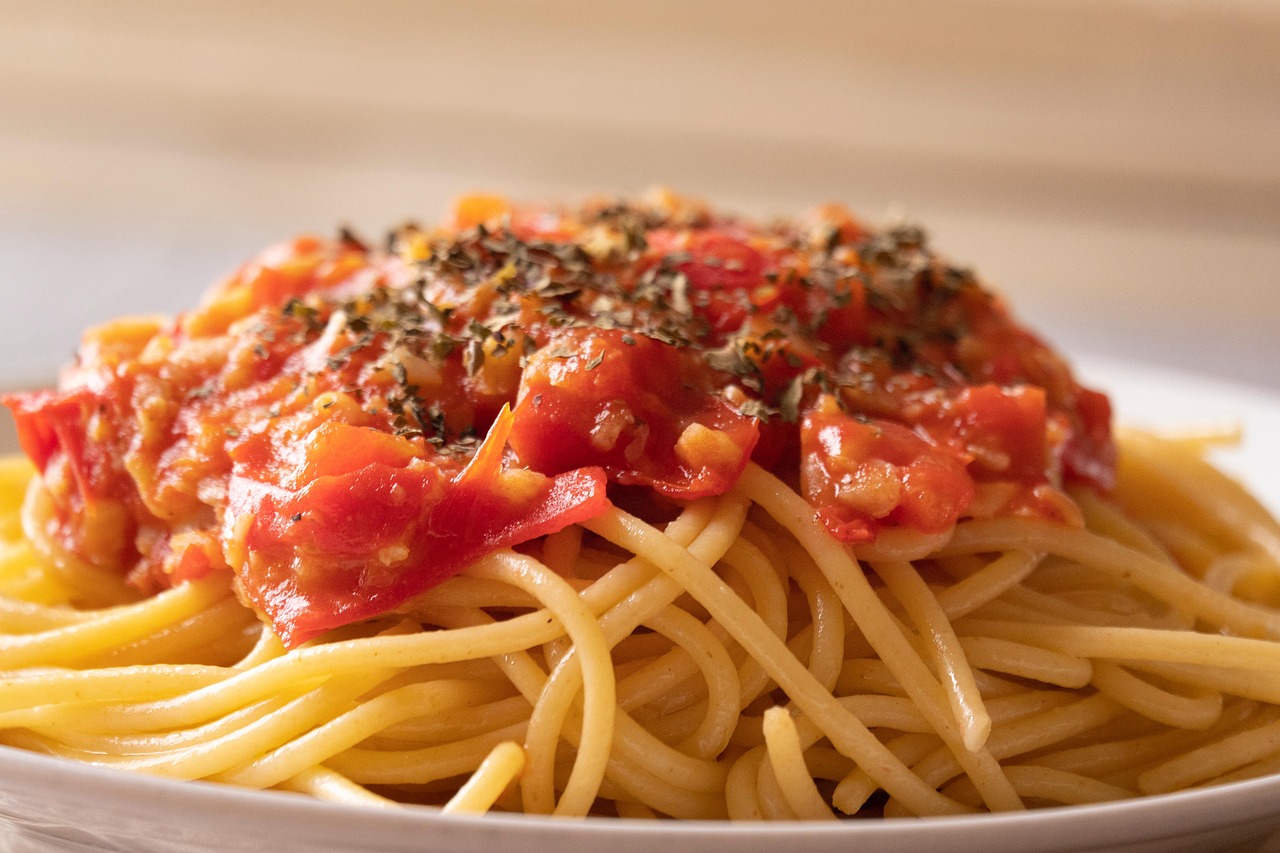 Pasta al pomodoro servita con basilico fresco e parmigiano grattugiato su un piatto bianco.